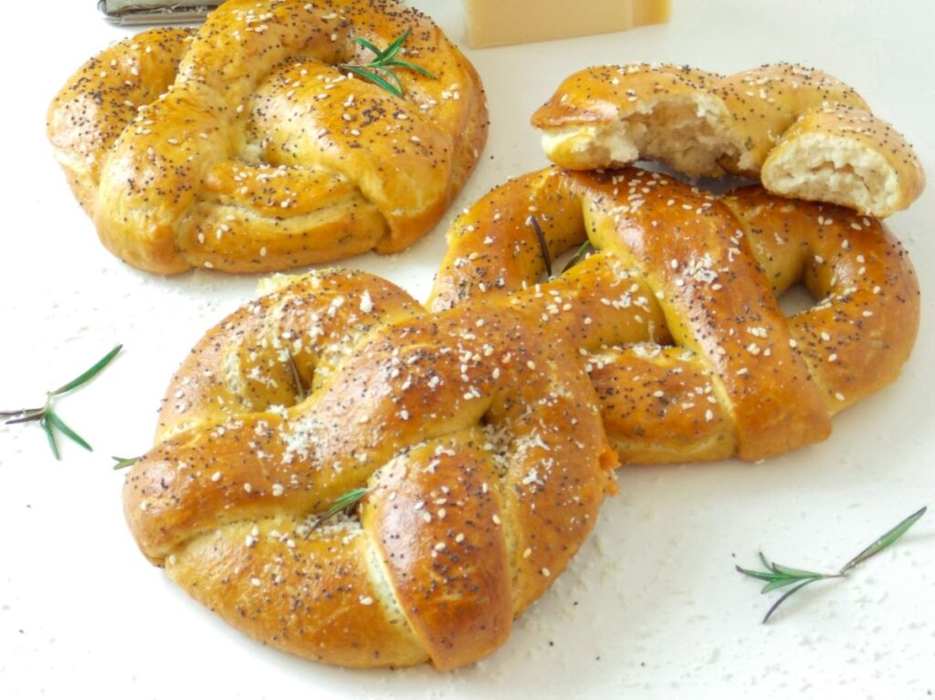 Covrigi pufoși umpluți cu brânză, așezați pe masă, cu un covrig rupt în spate care arată textura moale și brânza topită din interior