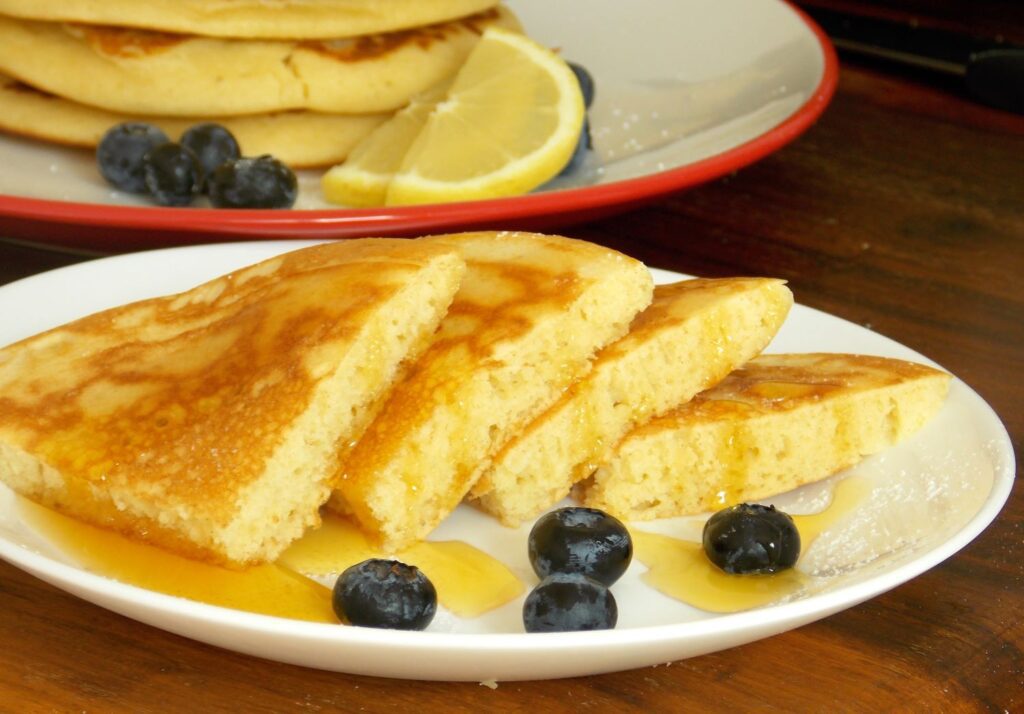 Pancakes clatite americane pufoase, in farfurie alaturi de miere in abundenta si afine 