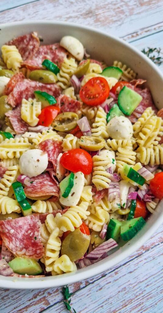 Bol generos de salata de paste cu mozzarella, salam si multe legume proaspete, precum rosii cherry, castraveti proaspeti si ceapa rosie 