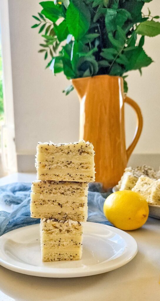 Turn de prăjituri cu foi fragede, mac și cremă de lămâie și vanilie, prezentat cu straturi elegante. Fiecare strat de foi fragede, ușor crocante, este umplut cu o cremă fină de lămâie și vanilie, iar decorul cu fulgi de cocos adaugă un aspect apetisant. 