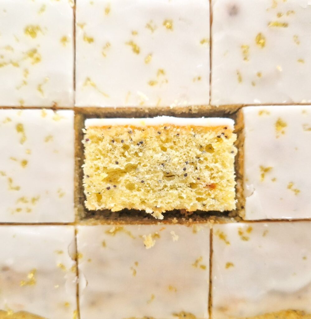 Prajitura cu lamaie si mac cu glazura de zahar portionata in bucati egale unde se vede textura si culoarea minunatat al acestei prajituri