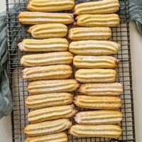 Prima imagine: Biscuiți lungi, dungați, aurii, dispuși pe un grătar de răcire, presărați ușor cu zahăr pudră. Aluatul lor bine definit păstrează forma în dungi datorită folosirii unui poș cu dui mare.