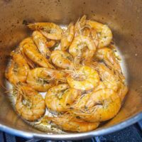 Creveți la tigaie, serviți în cochilie, cu un sos delicios de unt și usturoi, garnisiți cu felii de lămâie și pătrunjel proaspăt.