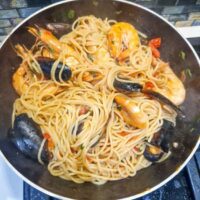 Spaghete cu creveți și scoici, gătite într-un sos aromat de usturoi, garnisite cu pătrunjel proaspăt și felii de lămâie.