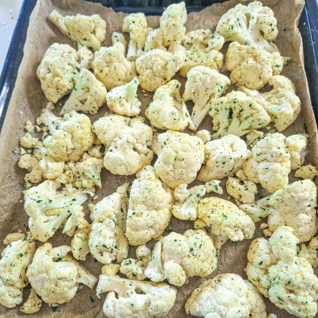 Buchețele de conopidă crude, condimentate cu ulei de măsline, usturoi și ierburi aromate, pregătite pentru cuptor.