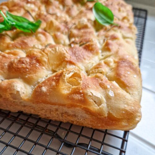 Focaccia cu fermentatie lenta, crusta crocanta si aurie, un cold foarte de aproape pentru a se vedea culoarea si crduta crocanta decorata cu rozmarin si busuioc