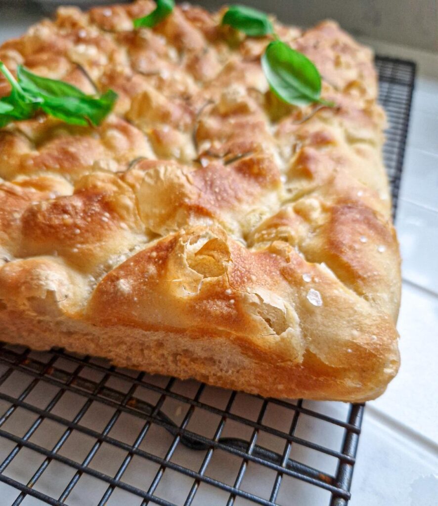 Focaccia cu fermentatie lenta, crusta crocanta si aurie, un cold foarte de aproape pentru a se vedea culoarea si crduta crocanta decorata cu rozmarin si busuioc
