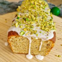 Chec cu fistic și glazură de lămâie pe blat de lemn, decorat cu glazura de zahăr pudră și fistic tocat