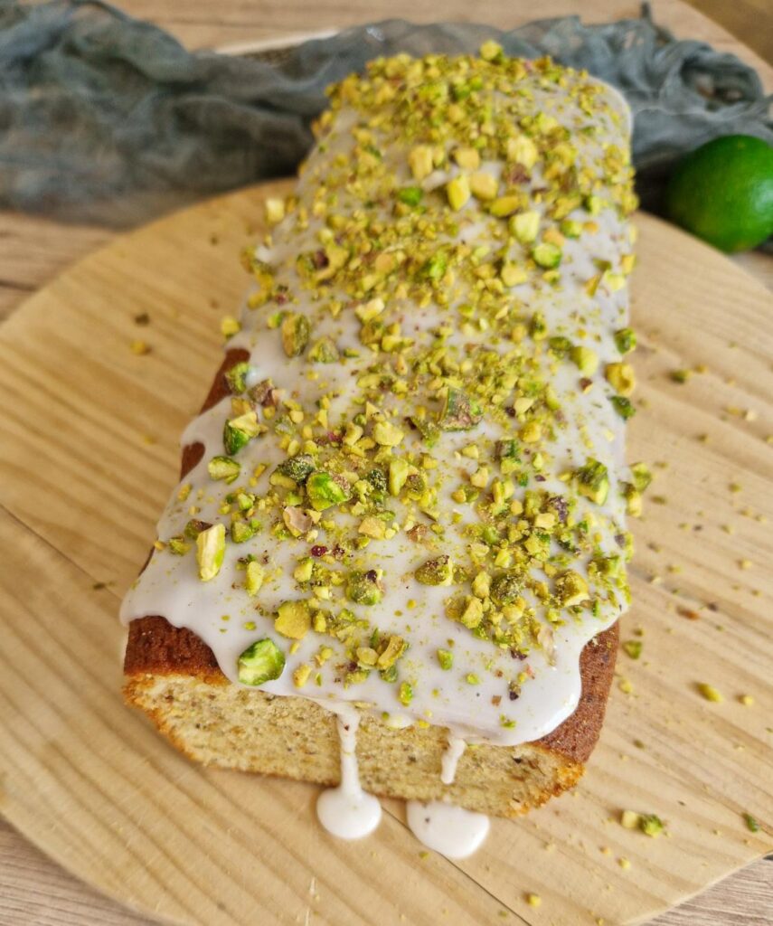 Chec cu fistic și glazură de lămâie pe blat de lemn, decorat cu glazura de zahăr pudră și fistic tocat