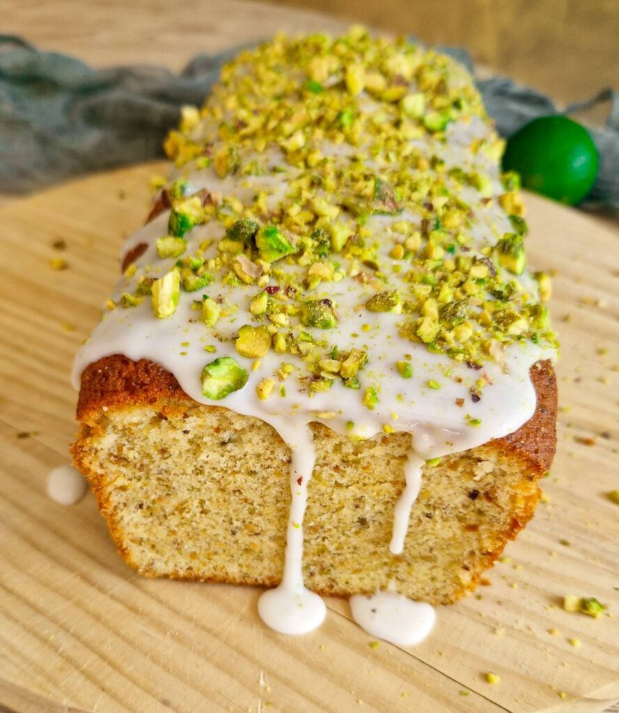 Chec cu fistic și glazură de lămâie pe blat de lemn, decorat cu glazura de zahăr pudră și fistic tocat