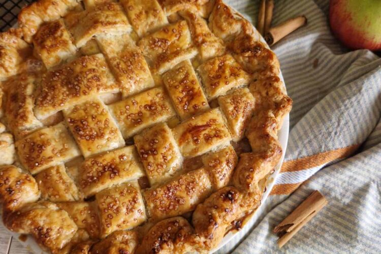 Apple Pie cu unt – rețeta clasică, pas cu pas - aurie abia scoasadin cuptor, cu un decor rustic cu prosop, baton de scortisoara, mere pe un gratar