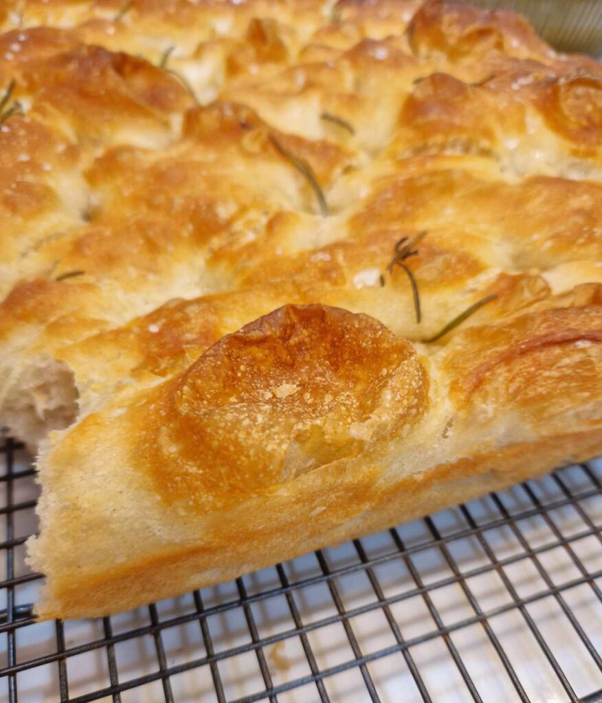 Detaliu de aproape al focaciei, evidențiind o bulă crocantă de coajă și textura moale din interior, cu rozmarin presărat deasupra.