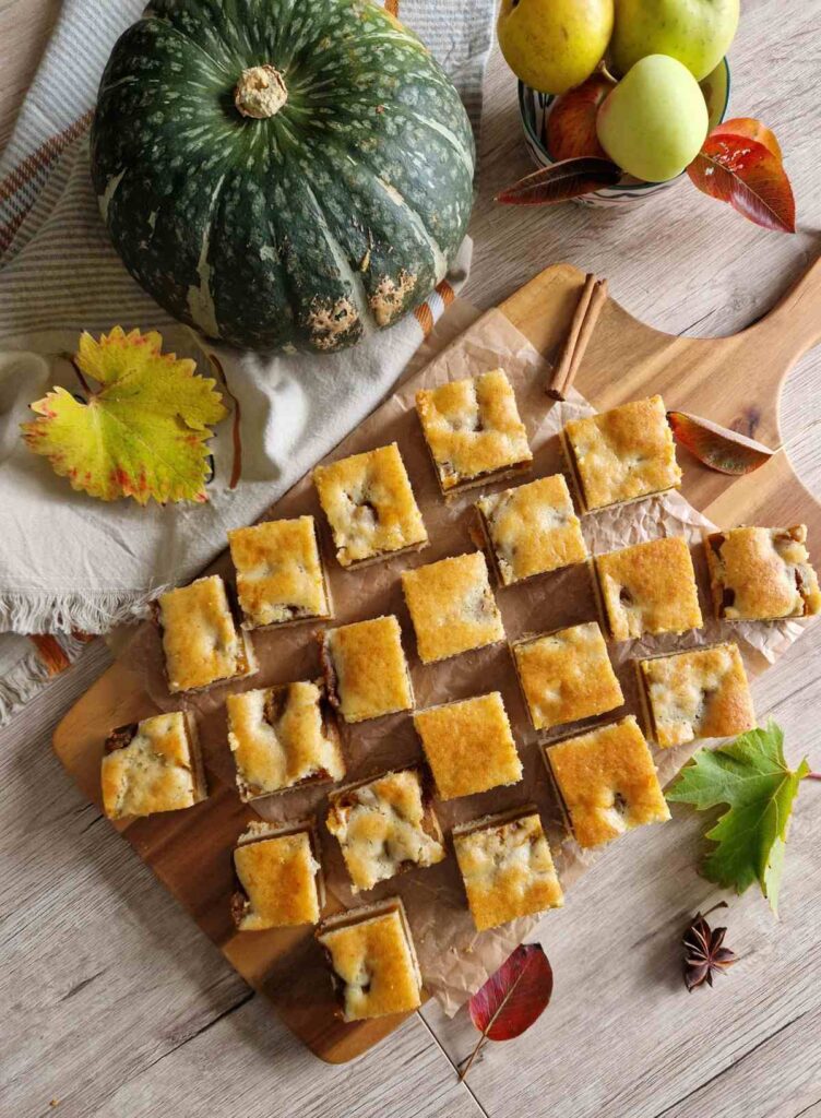 Prăjitură de toamnă cu dovleac, pe masă decorată cu frunze uscate și dovleac întreg