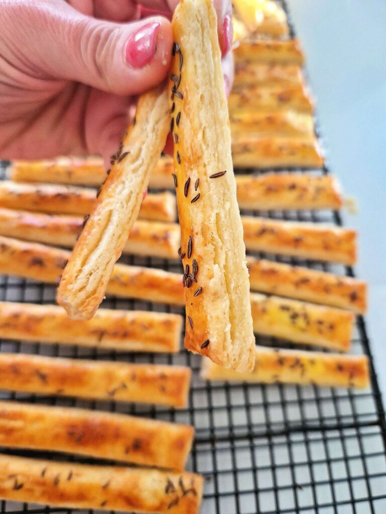 Sărățele cu untură și brânzeturi coapte, fragede si aurii, tinand doua in mana unde se vede clar textura de foietaj decasa