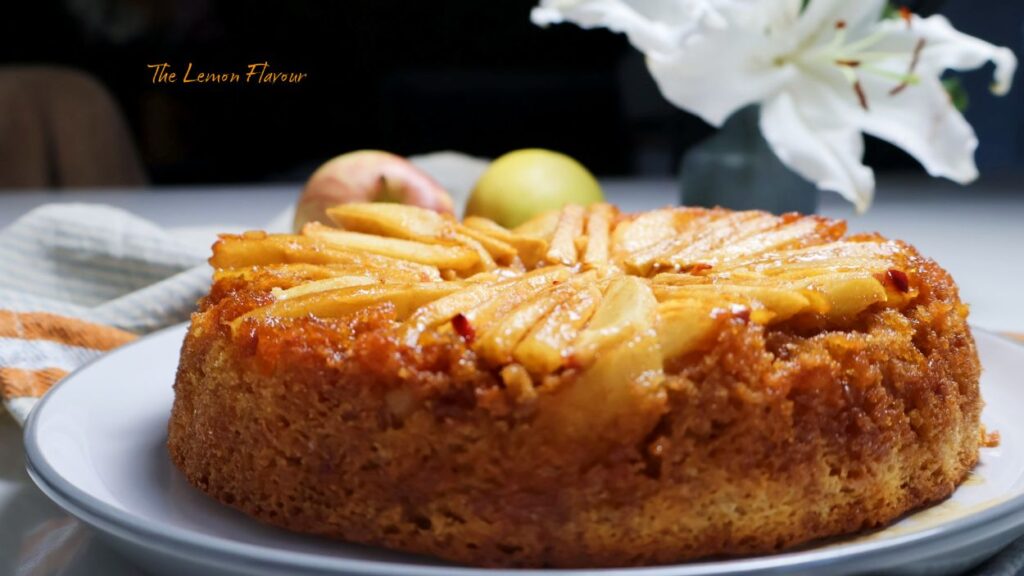 Prajitura Rasturnata cu mere pe platou, alaturi de un decor cu flori, mere si farfurii si furculite gata de servit