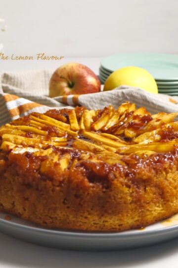 Prajitura Rasturnata cu mere pe platou, alaturi de un decor cu flori, mere si farfurii si furculite gata de servit