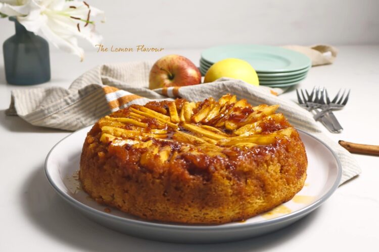 Prajitura Rasturnata cu mere pe platou, alaturi de un decor cu flori, mere si farfurii si furculite gata de servit