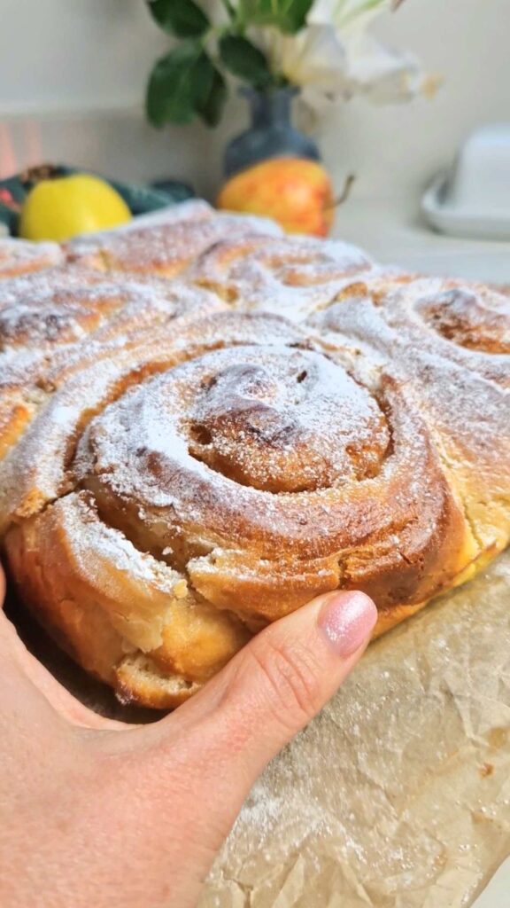Rulouri cu mere si scortisoara coapte unde se vede o mana care apuca sa rupa o bucata