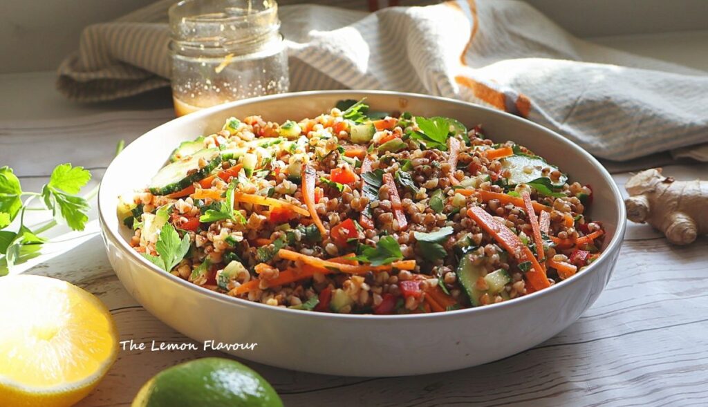 Salata de hrisca cu legume crocante precum morcovi, castraveti si dressing asiatic, cu decor de lamaie, lime si ghimbir iar in spate se vede borcanul de dressing 
